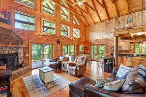 A spacious cabin with a stone fireplace, leather furniture, and large windows offering views of the outdoors.