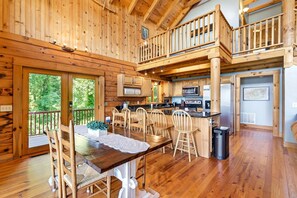 A wooden cabin interior with a dining area, kitchen, and a balcony.