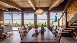 A dining area with a view of the beach, wooden beams, and a hanging light fixture. - Ocean Front on Miles of Sandy Beach! Dog Friendly! (Yachats)
