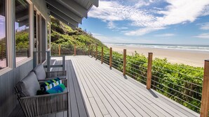 A wooden deck with a view of the beach, a railing, and a bench with cushions. - Ocean Front on Miles of Sandy Beach! Dog Friendly! (Yachats)
