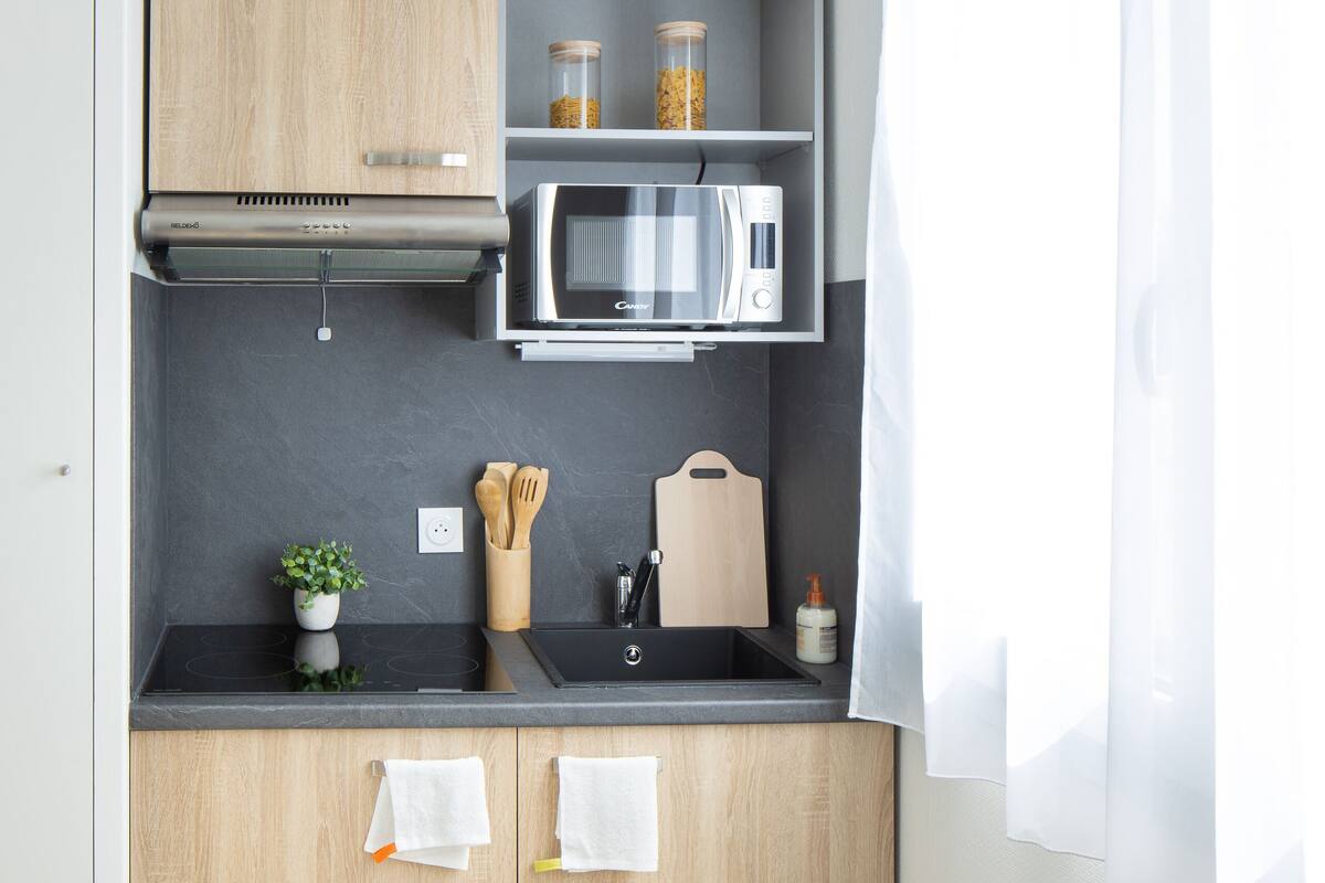 Een kleine keuken met houten kastjes, een magnetron en een klein aanrecht.