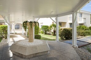 A covered outdoor area with a central column, white pillars, and a garden with various plants. - Residence Sweetly St Augustin (Bordeaux)