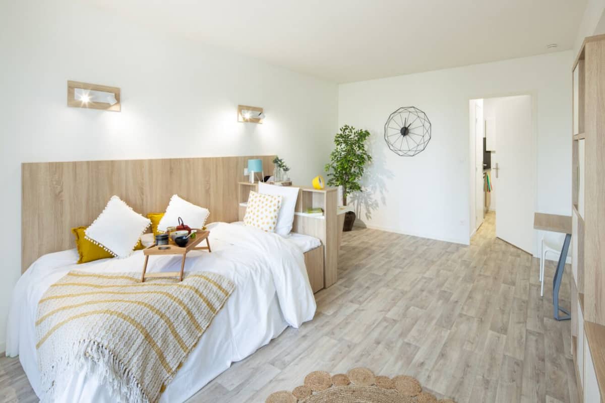 Een moderne slaapkamer met een houten hoofdbord, een nachtkastje met een lamp en een grote plant.