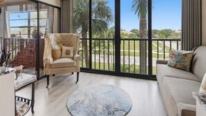 A spacious living room with a large window, a round rug, a beige armchair, and a sofa with decorative pillows.