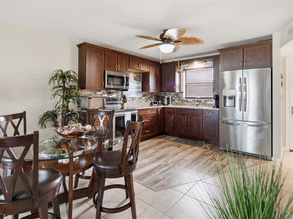 A modern kitchen with dark wood cabinets, stainless steel appliances, and a glass dining table.