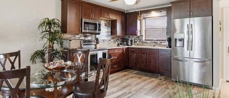 A modern kitchen with dark wood cabinets, stainless steel appliances, and a glass dining table.