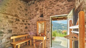 Una habitación rústica con paredes de piedra, un banco de madera, un escritorio con espejo y vistas al exterior.
