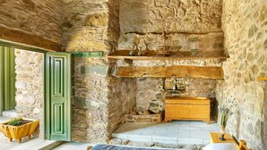 Una habitación rústica con paredes de piedra, una cama, un aparador de madera y un pequeño altar con velas.