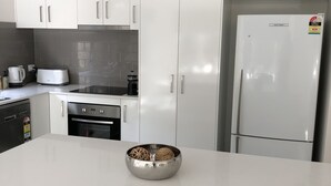 Une cuisine moderne avec des meubles blancs, un réfrigérateur en acier inoxydable, un grille-pain et un bol posé sur le plan de travail.