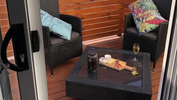 Une terrasse extérieure avec des meubles en osier, une table en verre et une clôture en bois.
