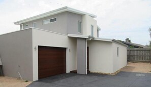 Een modern huis met twee verdiepingen, een garage, een overdekte oprit en een houten hek op de achtergrond.