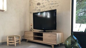 A modern living room with a flat-screen TV on a wooden TV stand, a small wooden stool, and a green glass vase. - Mas provençal La Serallère in the heart of olive groves (Venterol)