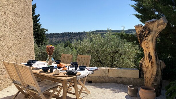 An outdoor dining area with a table set for two, surrounded by chairs, a vase with flowers, and a croissant. - Mas provençal La Serallère in the heart of olive groves (Venterol)