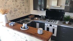 A modern kitchen with a stone wall backsplash, a wooden countertop, a gas stove, an oven, and a sink. - Mas provençal La Serallère in the heart of olive groves (Venterol)