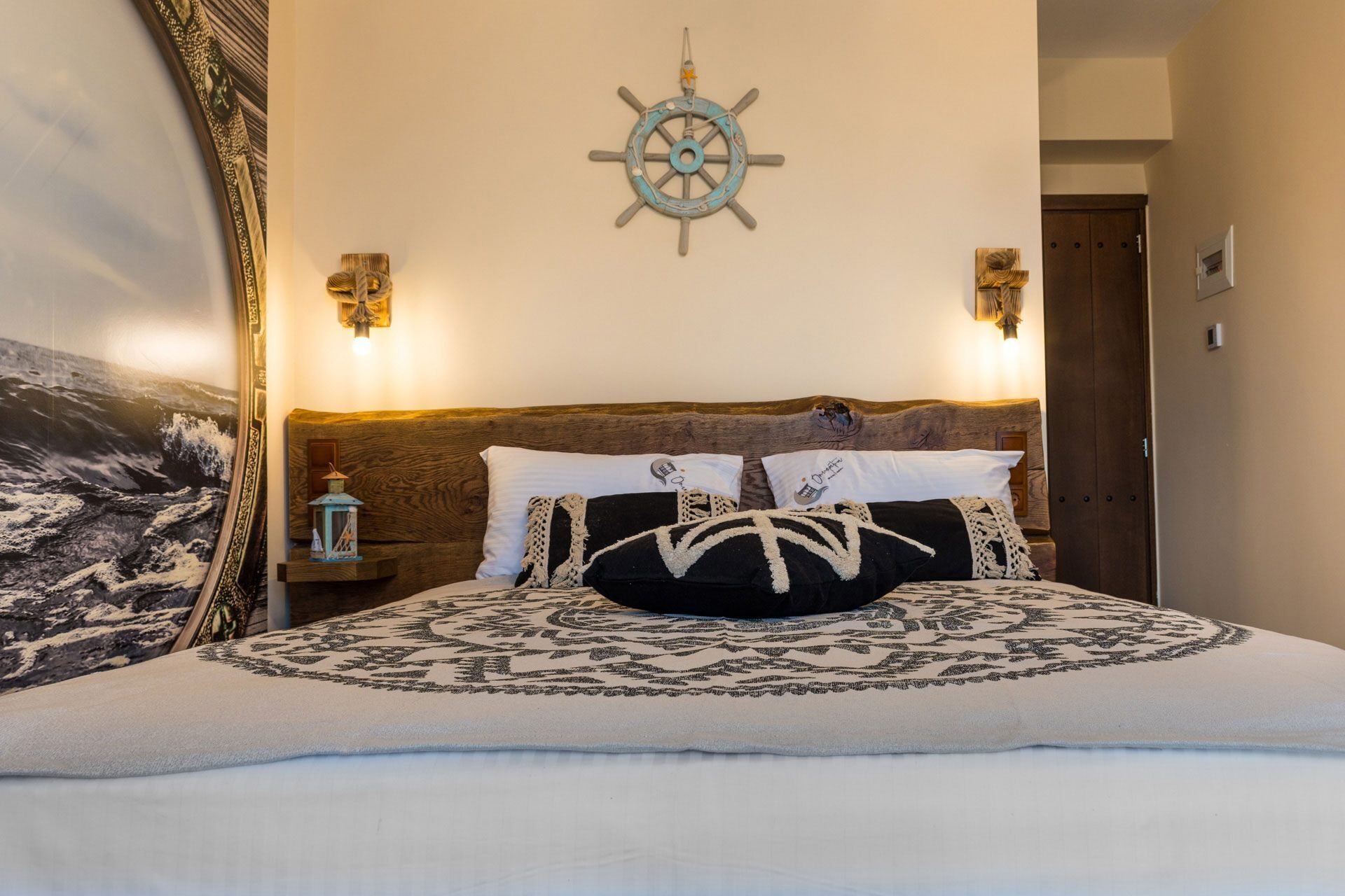 A bed with a nautical-themed headboard, a wall-mounted ship's wheel, and two wall sconces.
