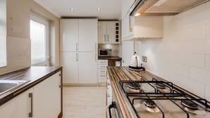 Una cocina moderna con armarios blancos, una estufa a gas, un microondas y un ventanal que proporciona luz natural.