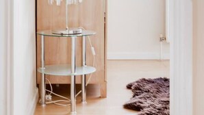 Una habitación con puerta de madera, una mesa de vidrio y un colgante de techo, además de una ventana con persianas.