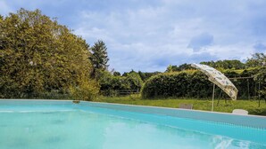Een zwembad met een helderblauw wateroppervlak, omringd door weelderige begroeiing en bomen.