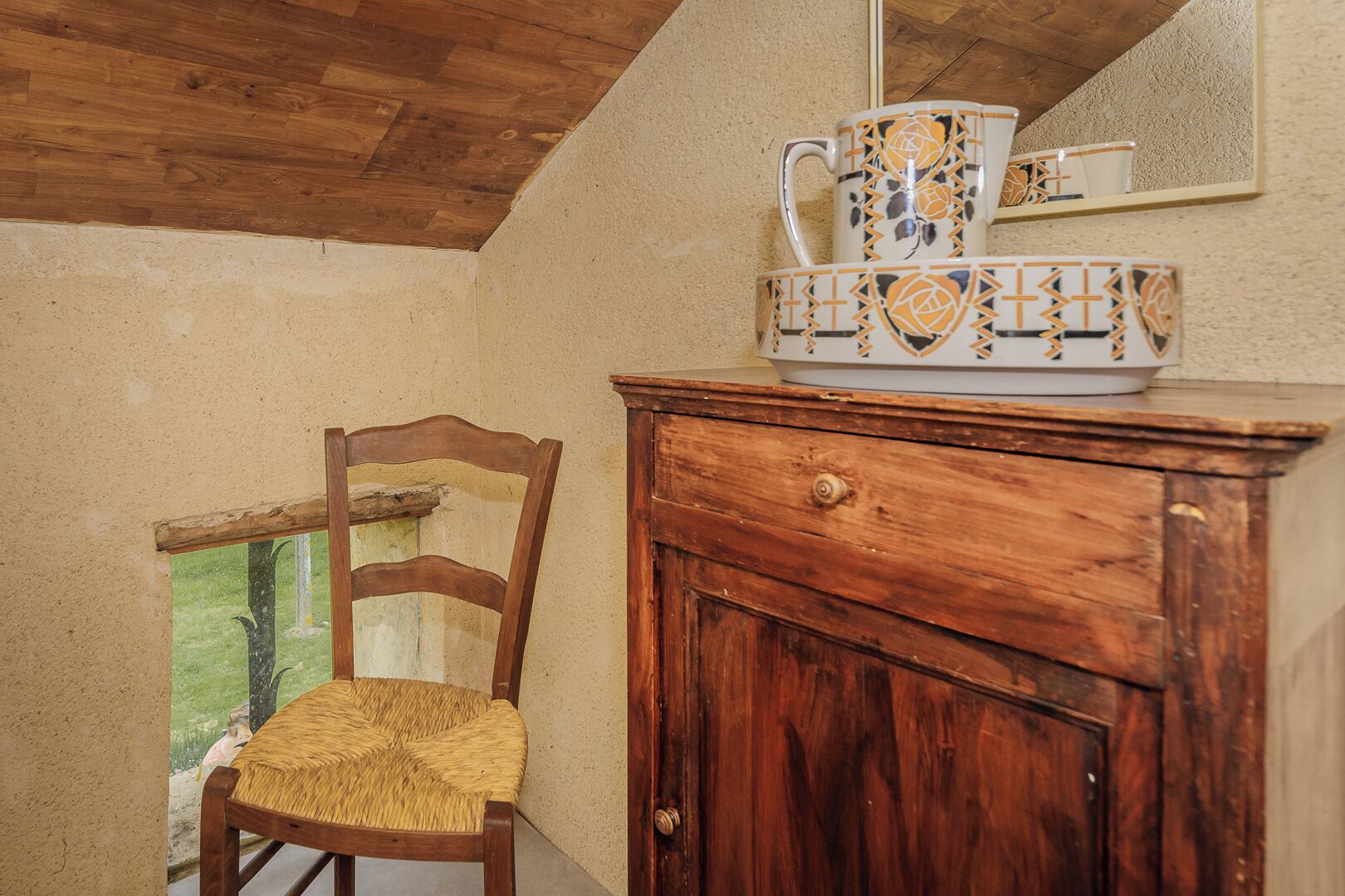 Ein rustikaler Holzstuhl mit gewebter Sitzfläche, ein Holzkabinent mit einer Schublade und eine Reihe von bunten Keramiktassen darauf.