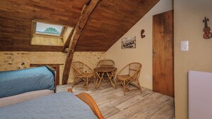 Een gezellig slaapkamer op zolder met een schuine kap, een klein raam, een bed, twee rieten stoelen, een ronde tafel en een deur.