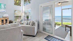Un soggiorno moderno con un'ampia porta-finestra scorrevole su un balcone, una ventola a soffitto e vista sull'oceano.