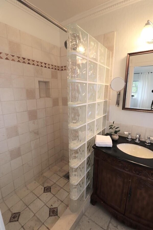 A bathroom with a glass shower enclosure, a wooden vanity, and a mirror with a light.