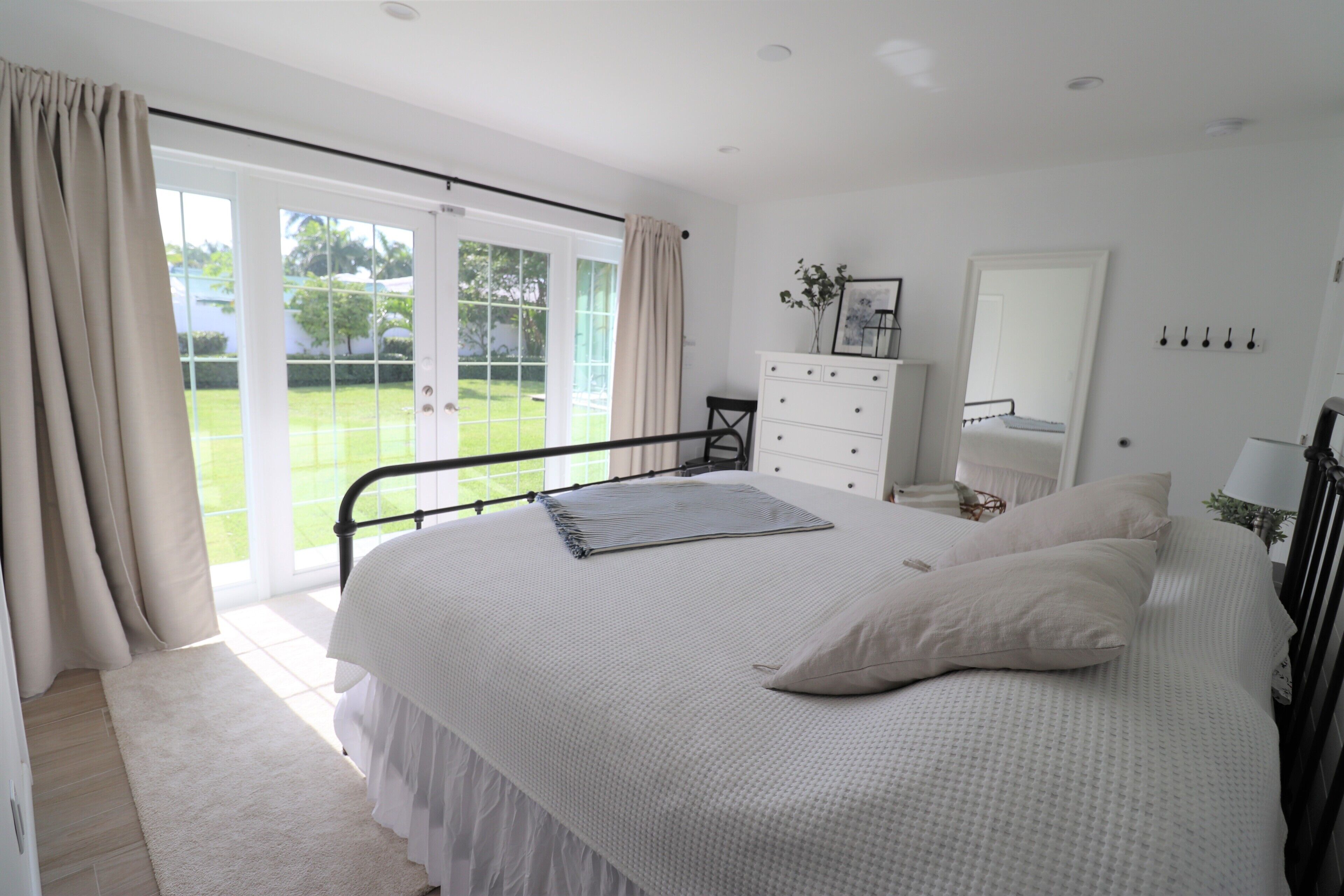 Ein Schlafzimmer mit einem großen Bett, einem Schminktisch, einem Spiegel und Blick auf den Garten durch die Schiebeglastür.