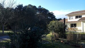 A residential area with a house featuring a tiled roof, a patio with outdoor furniture, and a large tree in the foreground. - House with two terraces (south and north) and direct access to the bike path. (Messanges)