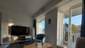 A modern living room with a flat-screen TV, a blue armchair, a wooden coffee table, and a sofa. - Apartment Meerliebe 🌅 2nd floor with balcony and sea view. 82m2 for 4 people + 🦮 (Prora (Binz))