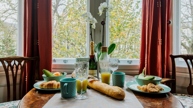 A breakfast table with croissants, a bottle of champagne, and a vase of white flowers. - The Suite, 82 Cathedral, Private Parking (Cardiff)