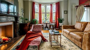 A cozy living room with a fireplace, a comfortable sofa, a dining table, and a bay window with curtains. - The Suite, 82 Cathedral, Private Parking (Cardiff)