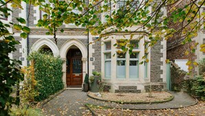 A building with a stone facade, a central arched entrance, and a small garden area with a pathway. - The Suite, 82 Cathedral, Private Parking (Cardiff)