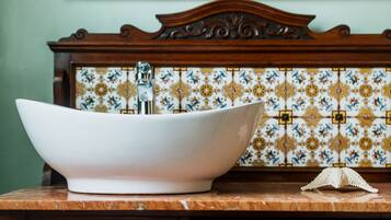 Une salle de bain dotée d’un grand lavabo sur pied blanc, d’un miroir avec un cadre doré et d’un pare-feu en carreaux.