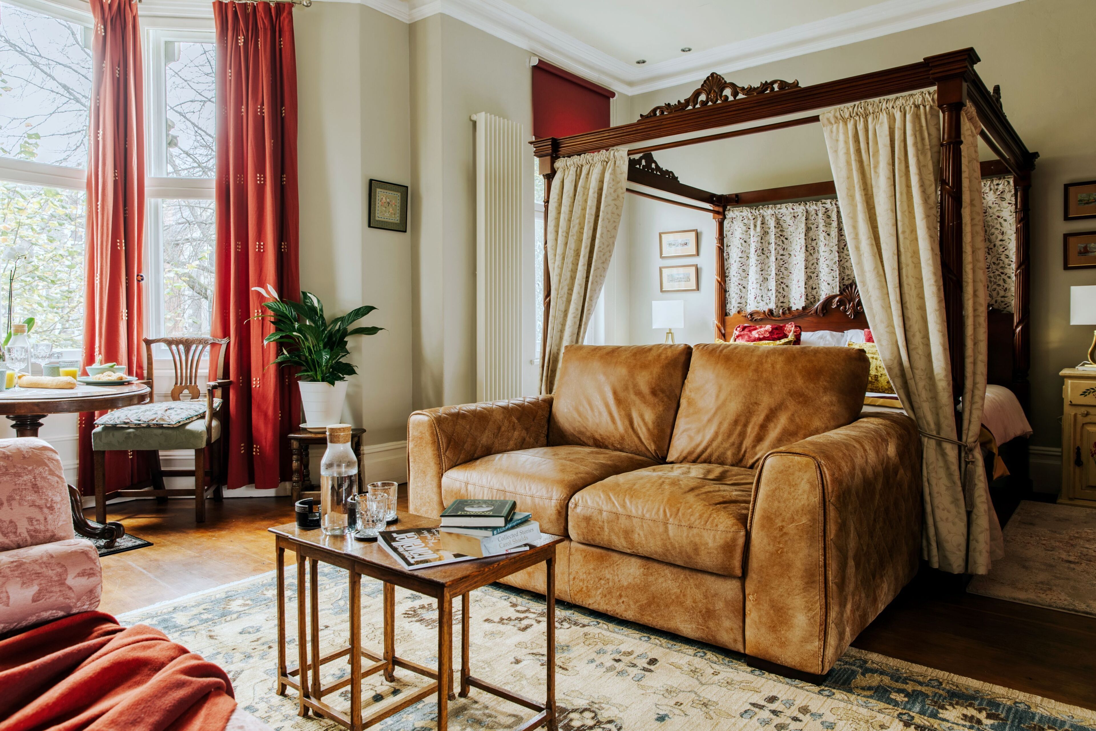A room with a four-poster bed, a leather sofa, a wooden coffee table, and a dining area with a table and chairs.