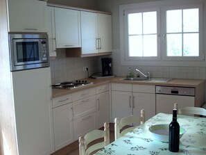 A kitchen with white cabinets, a microwave, a stove, a sink, and a dining table with chairs.