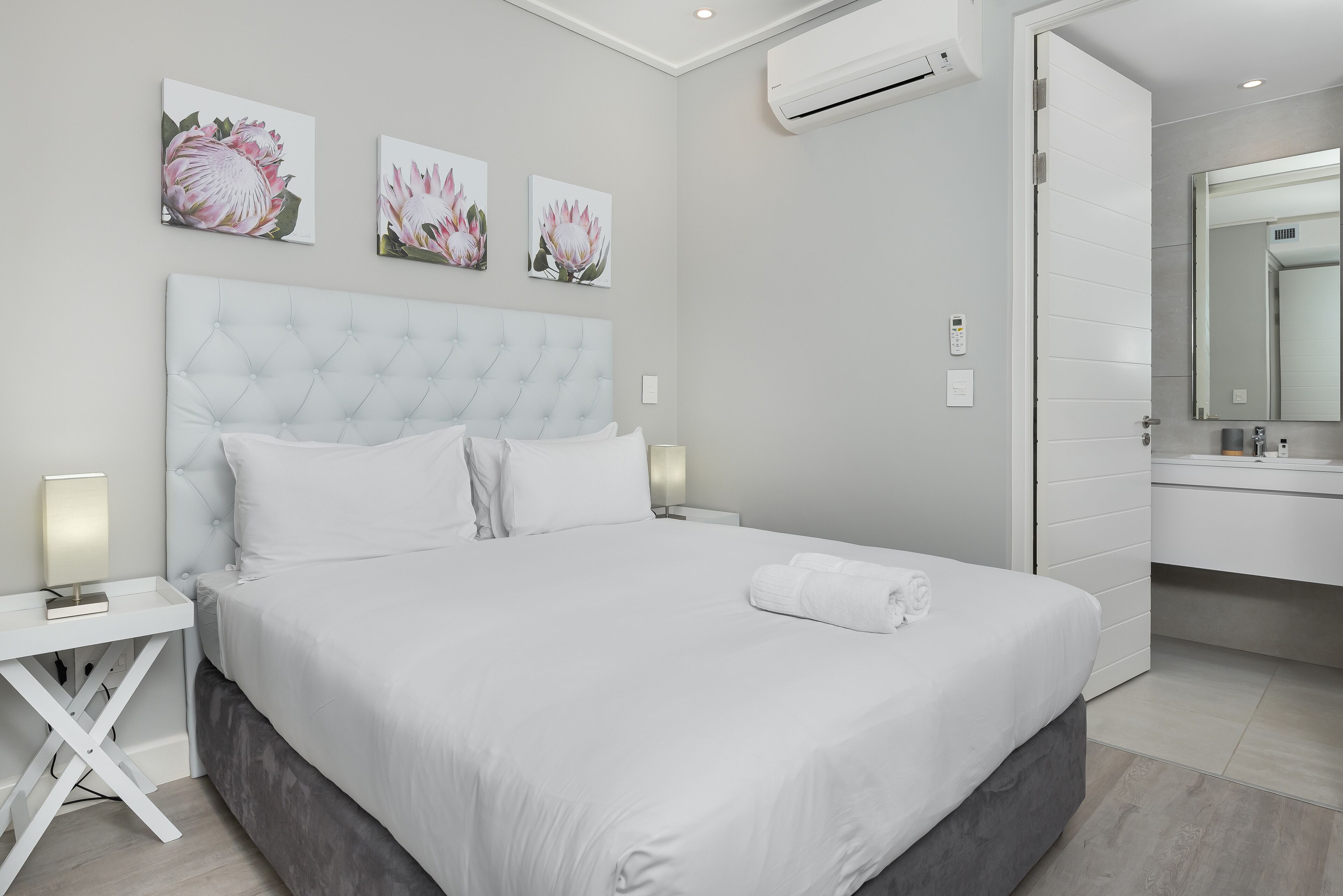 A modern hotel room with a large bed, a bedside table, a nightstand, and a wall-mounted air conditioner.