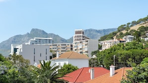 A coastal residential area with modern buildings, a red-roofed house, and mountains in the background.