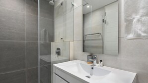 A modern bathroom with a glass shower enclosure, a white sink, and a large mirror.