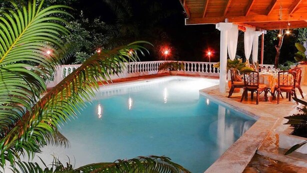 A nighttime pool area with a wooden deck, white railing, and tables set for dining. - Ace Holiday Room w. Private Bath in Colonial Villa (Sosúa)