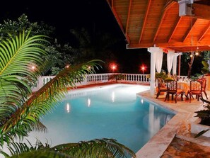A nighttime pool area with a wooden deck, white railing, and tables set for dining. - Ace Holiday Room w. Private Bath in Colonial Villa (Sosúa)