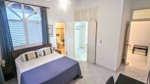 A bedroom with a bed, a ceiling fan, a window with curtains, and a bathroom visible through an open door. - Ace Holiday Room w. Private Bath in Colonial Villa (Sosúa)
