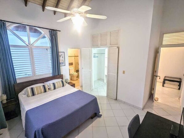 A bedroom with a bed, a ceiling fan, a window with curtains, and a bathroom visible through an open door.