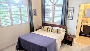 A neatly arranged bedroom with a bed, bedside tables, and a view through a window. - Ace Holiday Room w. Private Bath in Colonial Villa (Sosúa)