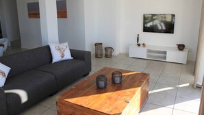 Ein modernes Wohnzimmer mit einem grauen Sofa, einem Holztisch, einer weißen TV-Konsole und dekorativen Körben.