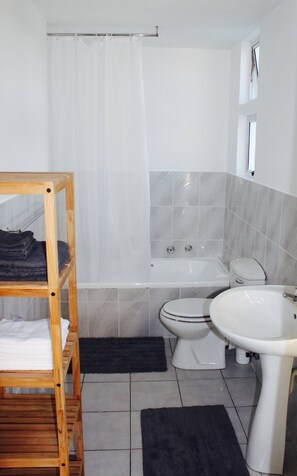 A bathroom with a wooden shelf, a bathtub, a toilet, and a sink.