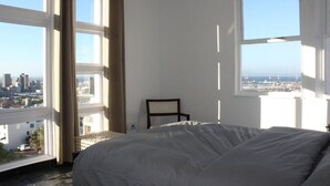 Ein Schlafzimmer mit einem Bett, einem Sessel und großen Fenstern mit Blick auf die Stadt.