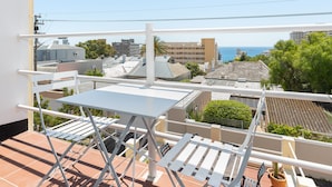Un balcon avec une table et des chaises blanches, donnant sur un quartier résidentiel et offrant une vue sur la mer.