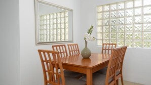 Un coin repas avec une table et des chaises en bois, un vase rempli de fleurs et deux fenêtres ornées de vitraux décoratifs.