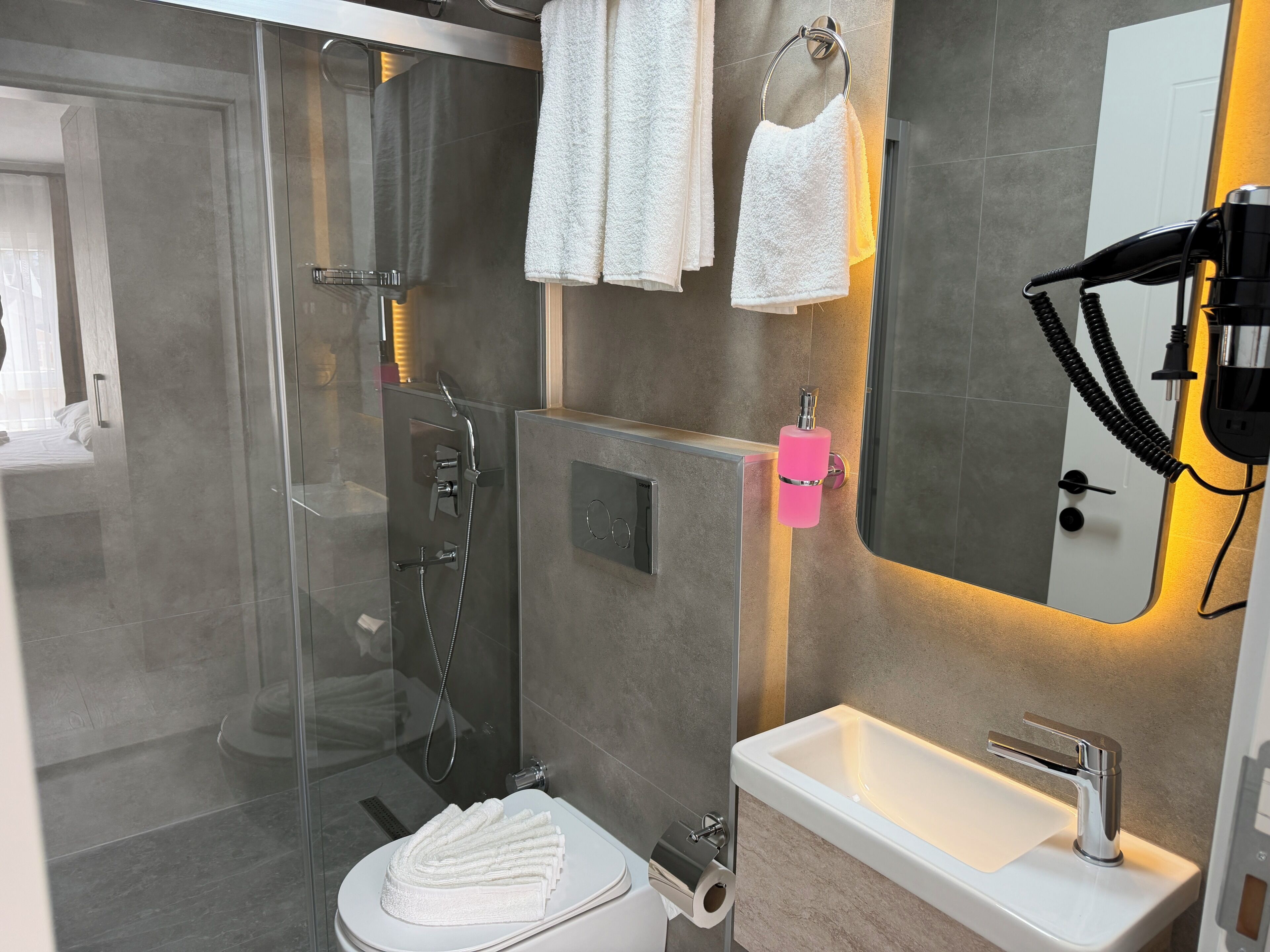 A modern bathroom with a glass-enclosed shower, a white sink, and a hairdryer on the wall.