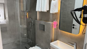 A modern bathroom with a glass-enclosed shower, a white sink, and a hairdryer on the wall.